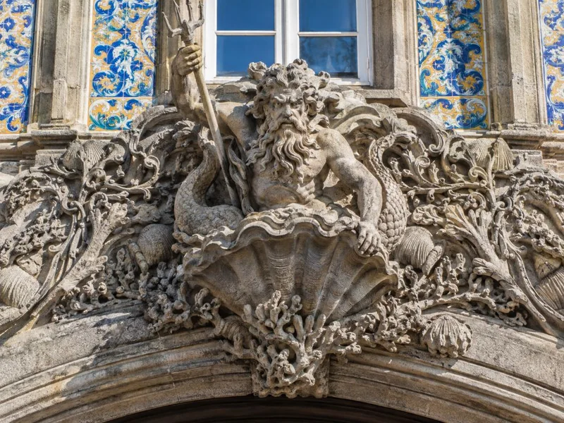An ornate carved stone arch with a mythical triton emerging from a shell beneath a tiled window