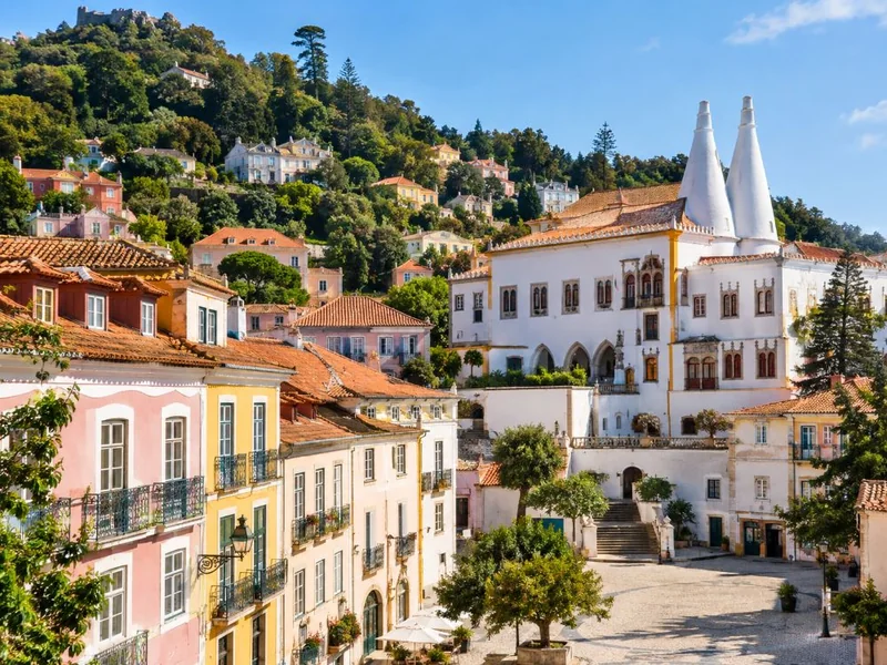 Pastel houses with iron balconies below a white palace with two tall conical chimneys