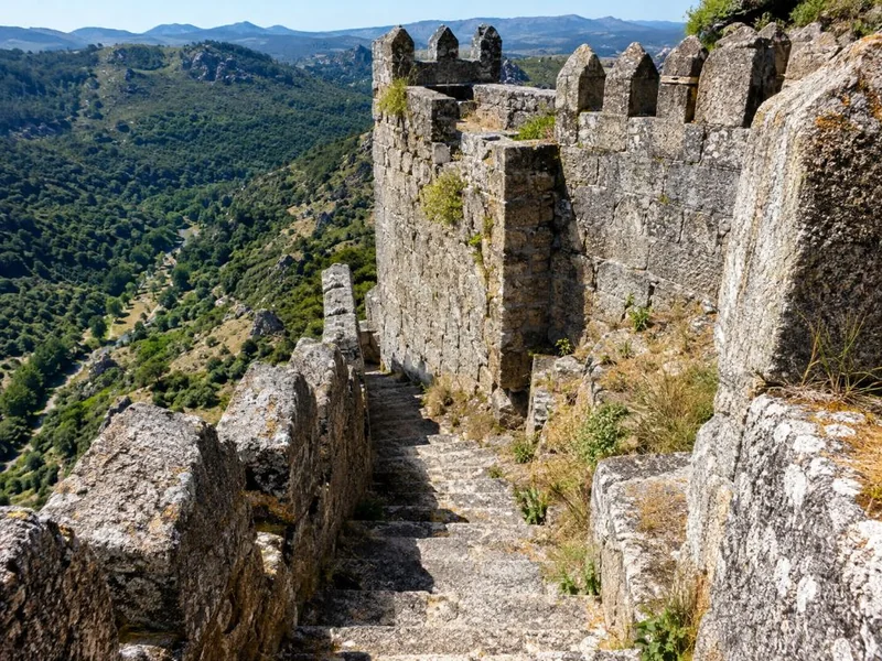 A steep stone stairway along medieval granite battlements above a forested valley